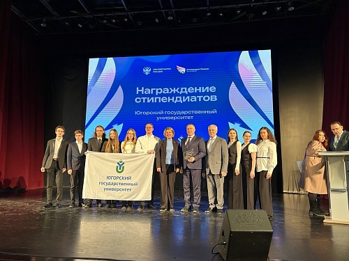 На сцене стоит группа людей. Часть из них держит белый флаг с изображением зелёного логотипа, под которым надпись 