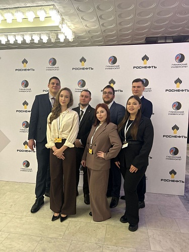 На фотографии группа из семи человек стоит перед баннером. На баннере повторяются логотипы 