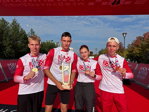 Четыре студенты ЮГУ – три парня и девушка - победители Международного Когалымского полумарафона стоят рядом на красной дорожке с медалями и кубком