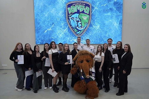 На фотографии изображена группа людей, стоящих перед большим экраном с логотипом хоккейного клуба 