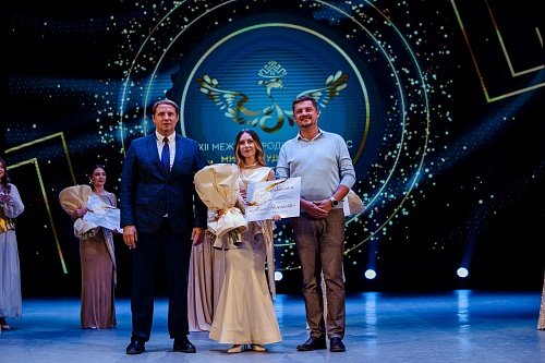 Студентка ЮГУ стоит на сцене, держа в руке букет цветов и диплом «Мисс нежность», который завоевала на Международном конкурсе «Мисс студенчества Финно-Угрии - 2025», с ней рядом стоят организаторы