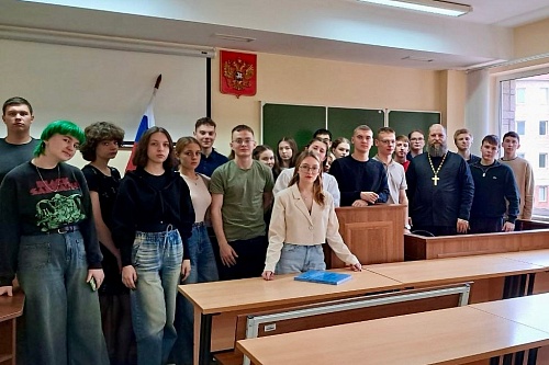 На фотографии изображена группа из примерно двадцати молодых людей и одного мужчины в рясе священника, стоящих в, предположительно, аудитории или зале суда.На заднем плане виден флаг России и герб России, висящий на стене. За группой людей находится белая