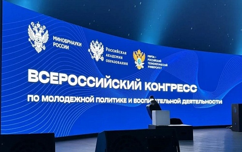 На изображении показана сцена с большим экраном на заднем плане. На экране отображается логотип Министерства науки и высшего образования Российской Федерации, логотип Российской академии образования и логотип МИРЭА - Российского технологического университ